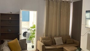A living room with a beige sofa, a wooden coffee table, and a chandelier. There is a bookshelf, a potted plant, and a view of the outside through a door. - Traditonal House - Etihad -Games Room-Free Parking (Manchester)