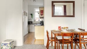 Un coin repas avec une table et des chaises en bois, une cuisine à l’arrière-plan et un miroir au mur.