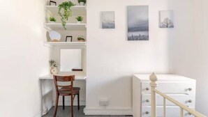 Une pièce avec un bureau blanc, une chaise, une commode blanche et un escalier avec une rampe blanche.