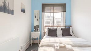 Une chambre à coucher comprenant un lit, une table de chevet, une fenêtre avec des stores et des œuvres d’art murales.