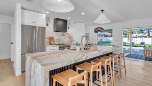 Una cocina moderna con una isla de mármol, electrodomésticos de acero inoxidable y taburetes de madera.
