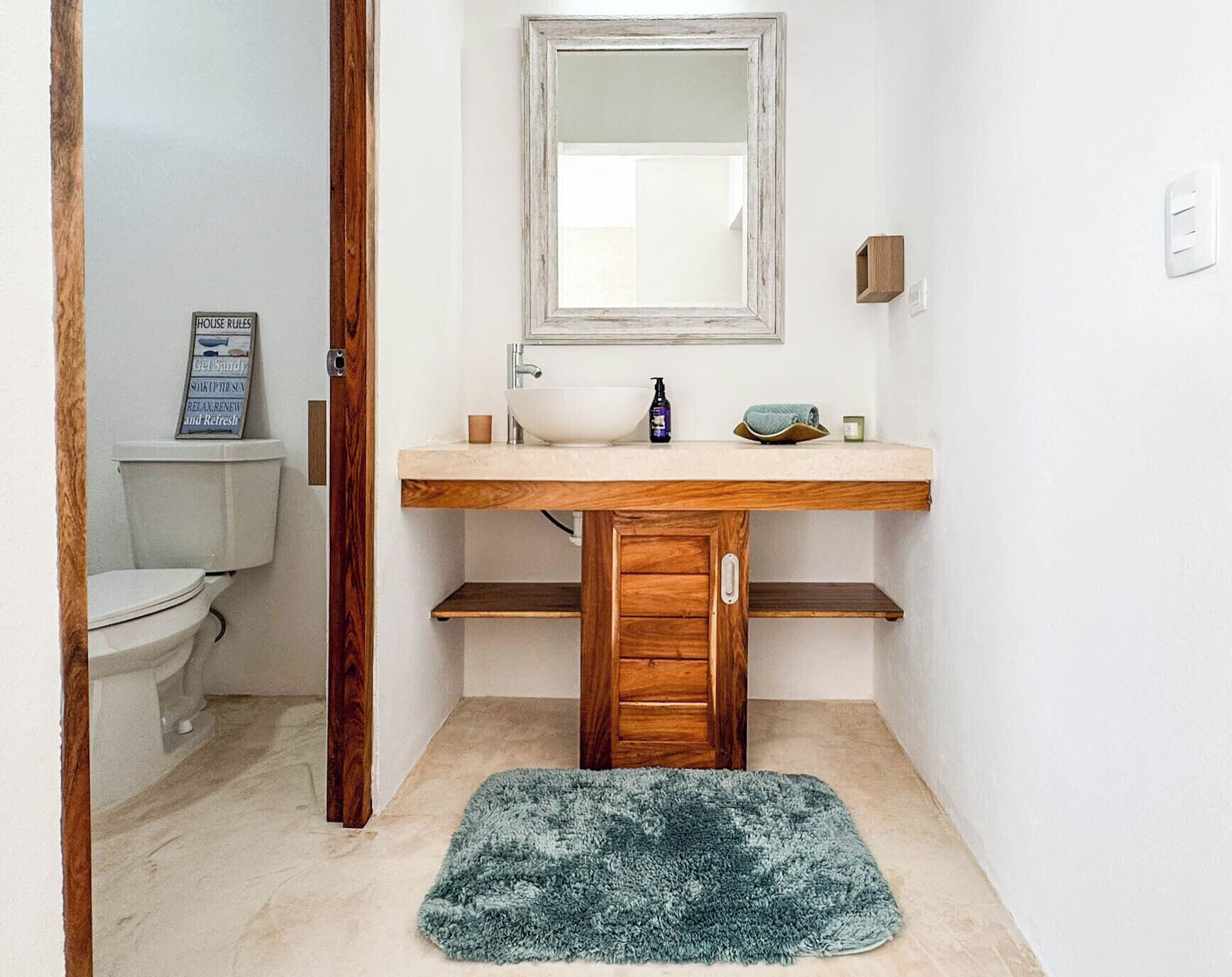 Ein Badezimmer mit einem Holz-Waschtisch, einem weißen Waschbecken, einem Spiegel, einer Toilette und einem blauen Teppich.