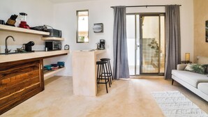 A modern living room with a sofa, a coffee table, and a kitchen area with a counter and bar stools. - Aria (El Cuyo)