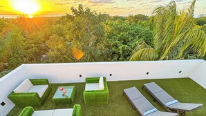 A rooftop terrace with green artificial grass, white and grey lounge chairs, and a glass table with red flowers. - Aria (El Cuyo)