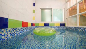 A swimming pool with a green inflatable ring, tiled walls with a rainbow pattern, and a window with frosted glass. - Gapyeong Gabom Kids Poolvilla Pension (Gapyeong)