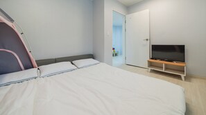 Une chambre à coucher avec un lit, un téléviseur posé sur un meuble, une armoire et une porte donnant sur une autre pièce.
