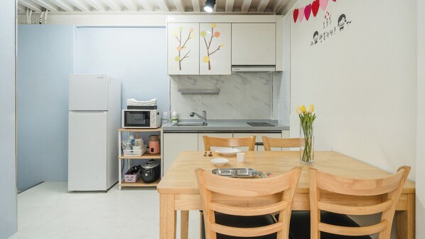 A compact kitchen with a refrigerator, microwave, and sink. There is a dining table with chairs and a vase of flowers. - Gapyeong Gabom Kids Poolvilla Pension (Gapyeong)