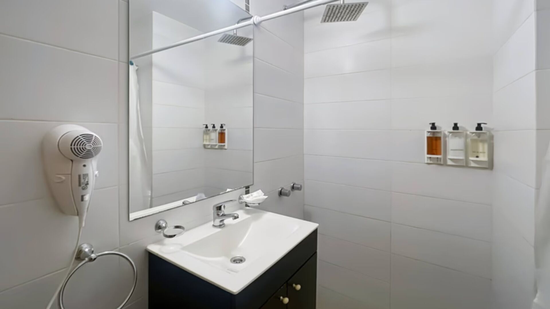 Een moderne badkamer met een witte wastafel, een föhn en toiletartikelen aan de muur.