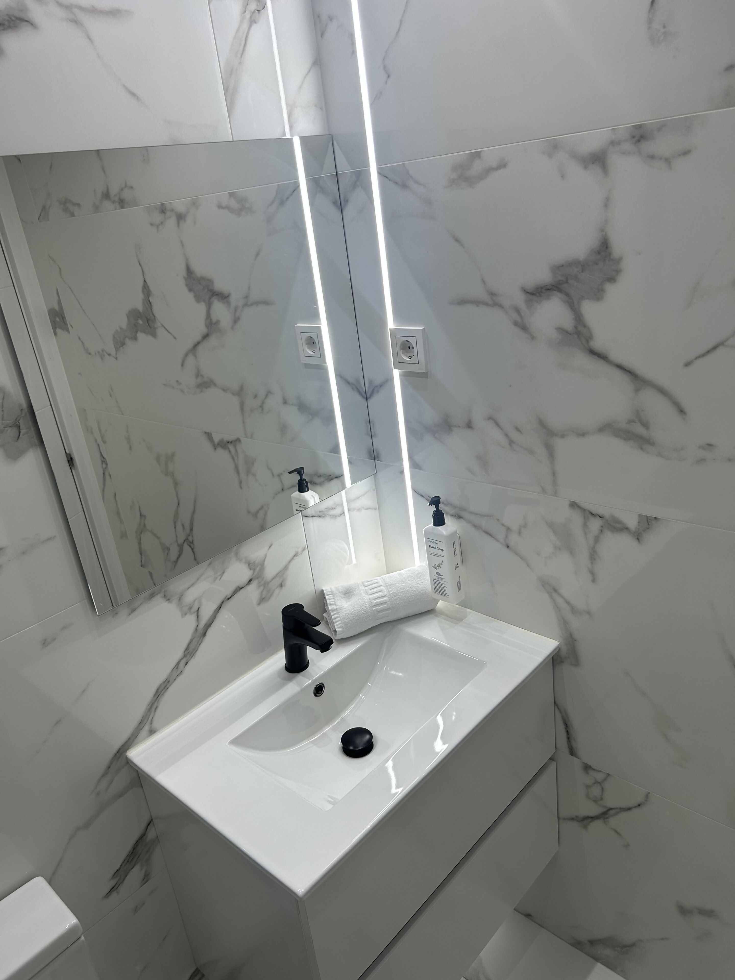 Un baño con lavamanos de mármol blanco, grifo negro, espejo y toalla.