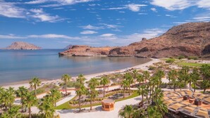 A coastal resort with a beach, palm trees, and a mountainous backdrop.
