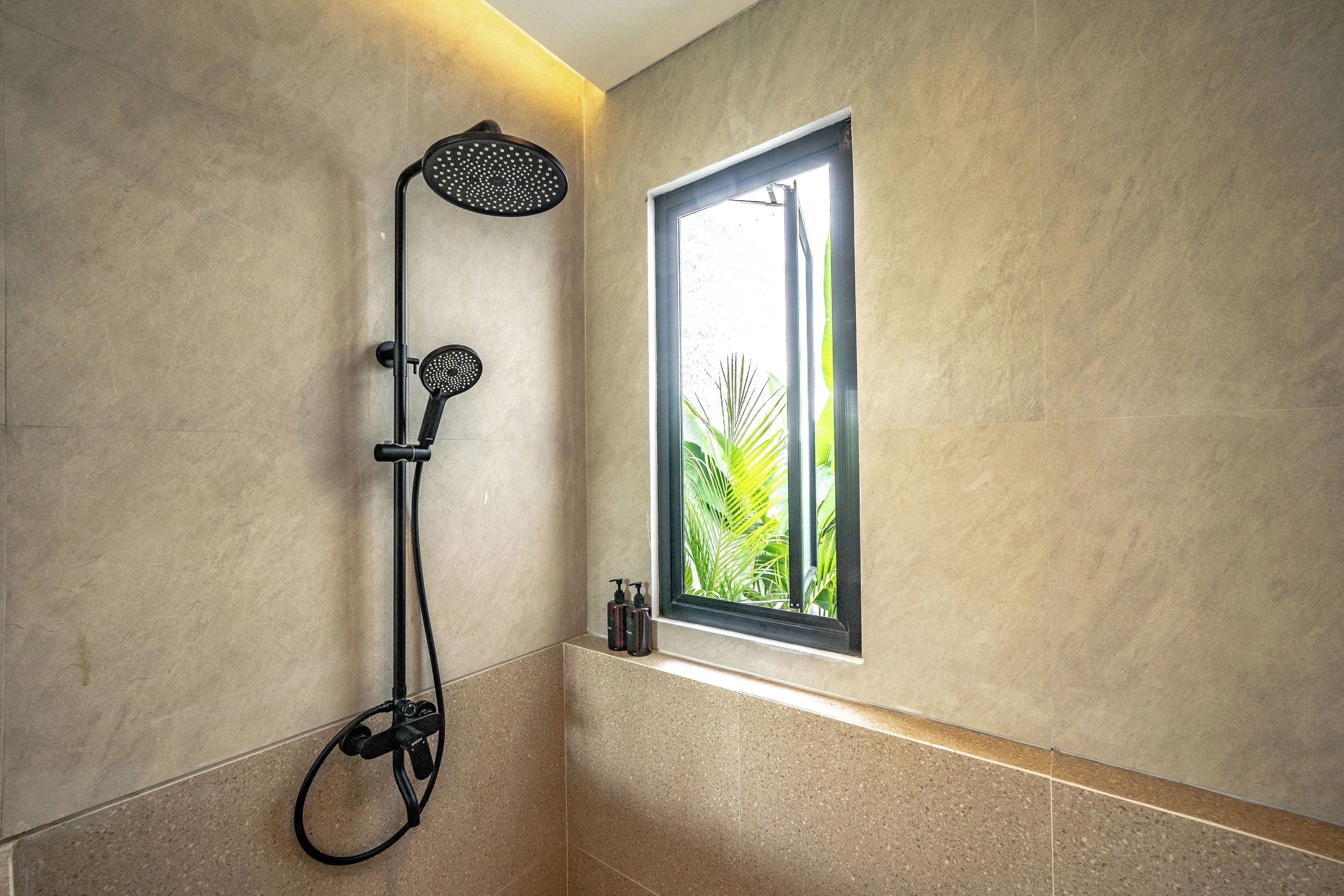 Un baño moderno con ducha, una ventana con vistas a follaje y un estante pequeño con artículos de aseo.