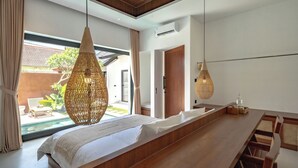 A modern bedroom with a long wooden bed, a hanging woven light fixture, and a view of a courtyard with a pool. - Casa Umari (Canggu)