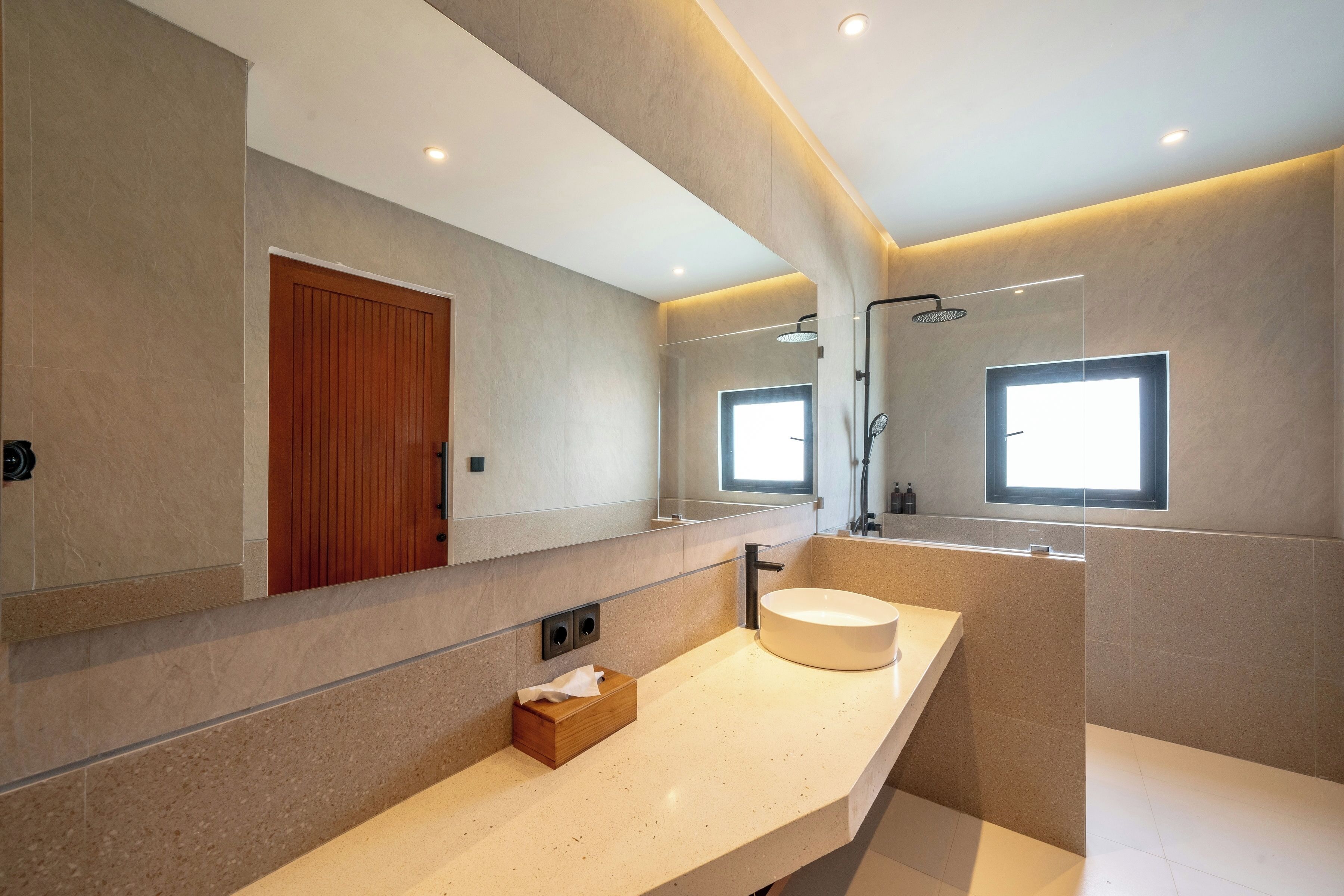 Une salle de bain moderne avec un grand miroir, une porte en bois, un lavabo rond et un espace douche.