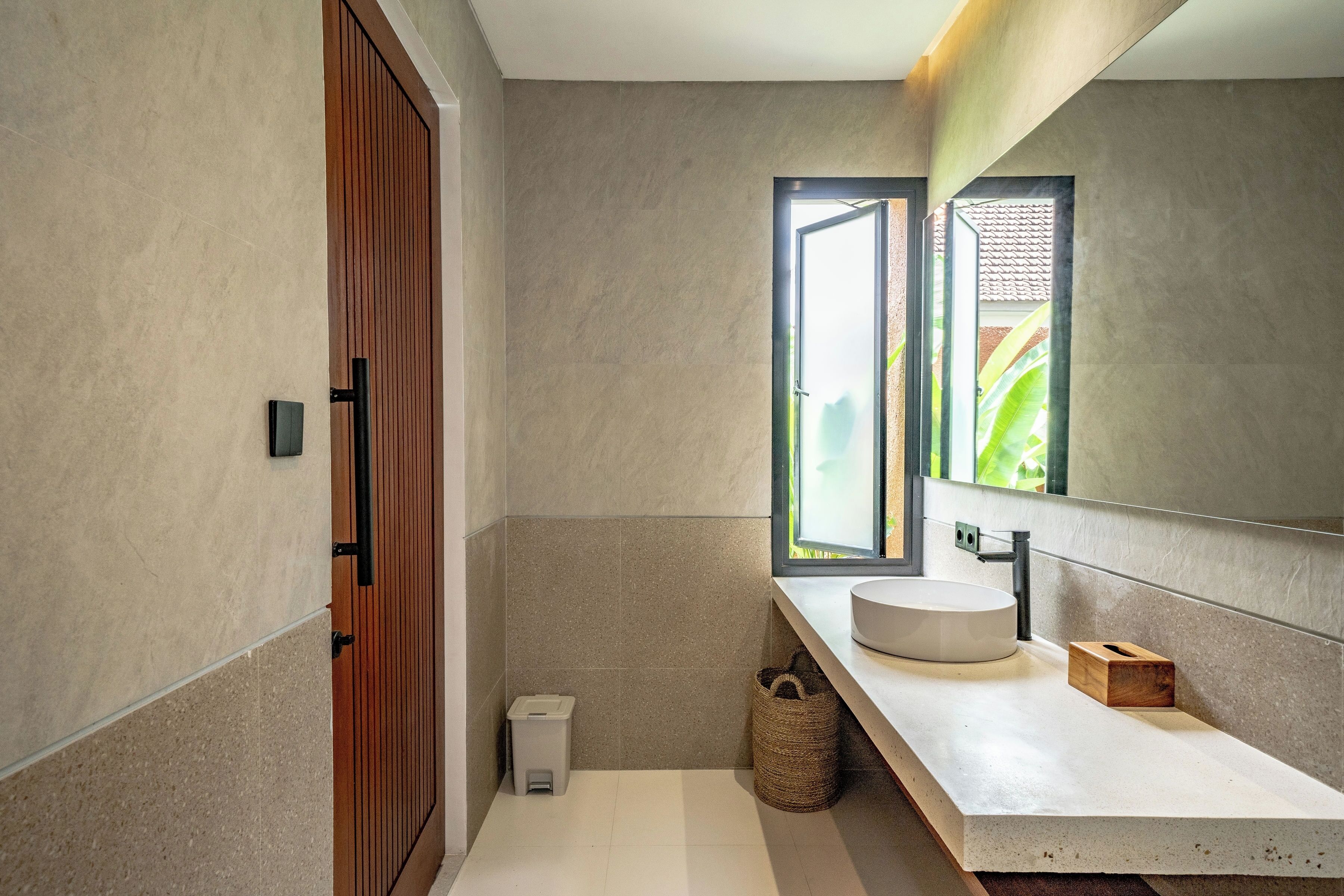 A modern bathroom with a large mirror, a round sink, and a wooden door.