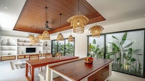 A modern kitchen with a wooden ceiling, white cabinetry, and a large island with a fruit bowl. - Casa Umari (Canggu)