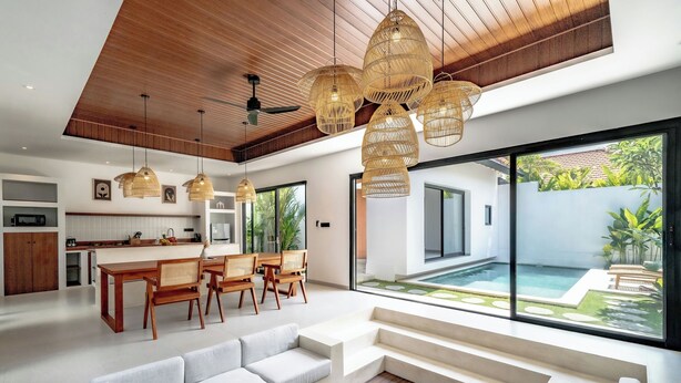 A modern living room with a large sofa, dining area, and a view of a swimming pool. - Casa Umari (Canggu)