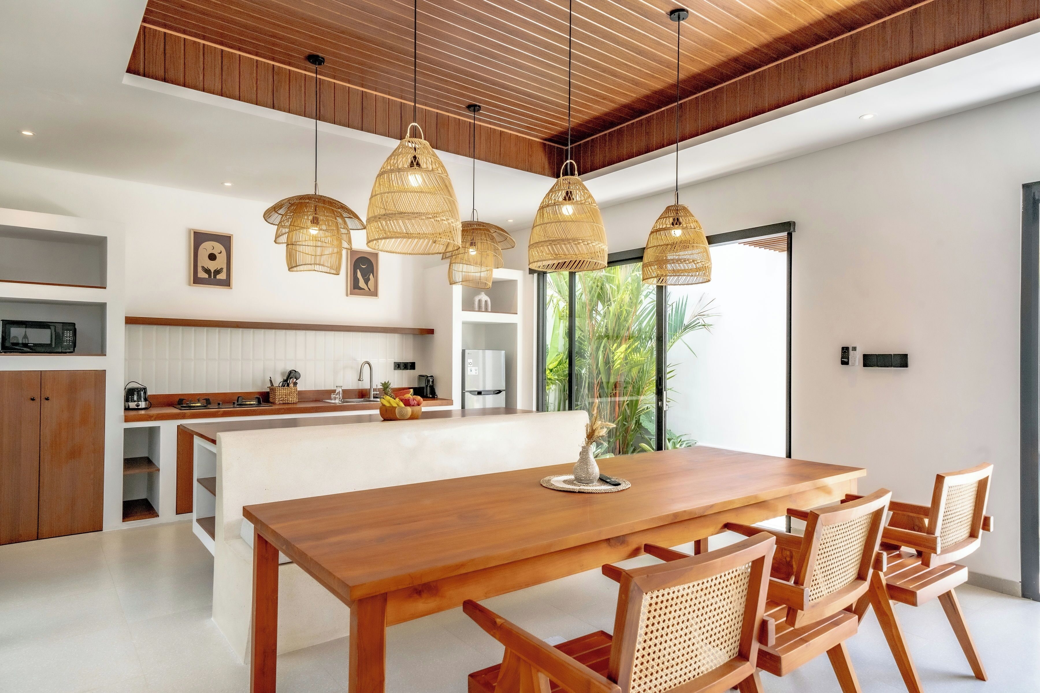A modern kitchen with a wooden dining table and chairs, pendant lights, and a view of the outdoors.