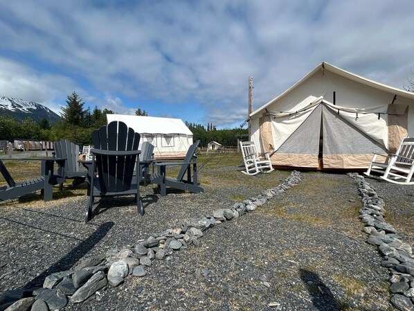 Un camping con dos tiendas de campaña, una mesa de madera y sillas tipo Adirondack.