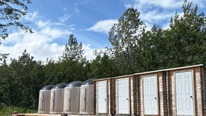 Draagbare toiletten met witte deuren, opgesteld in een rij op een houten platform.