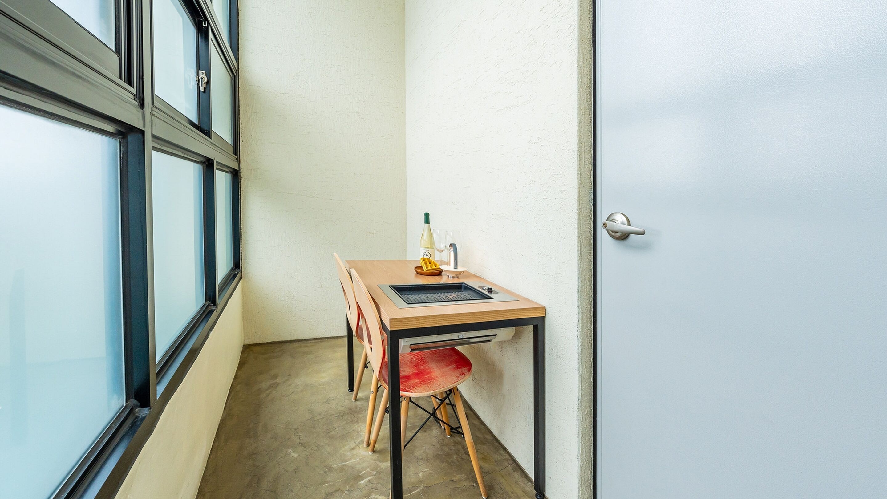 A small room with a wooden table, a red chair, a bottle of wine, and two glasses on the table.