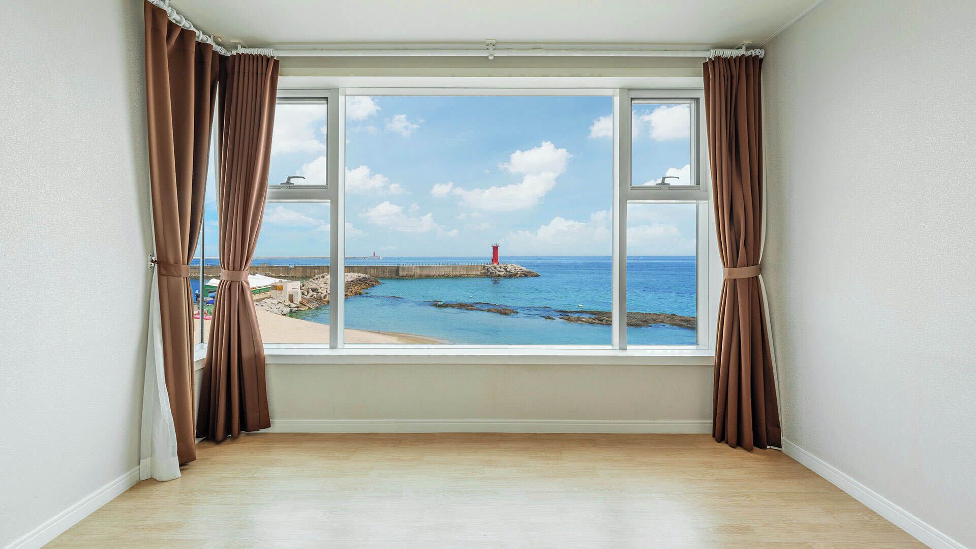 Una habitación con un ventanal grande que ofrece vistas costeras, con un faro y un litoral rocoso.