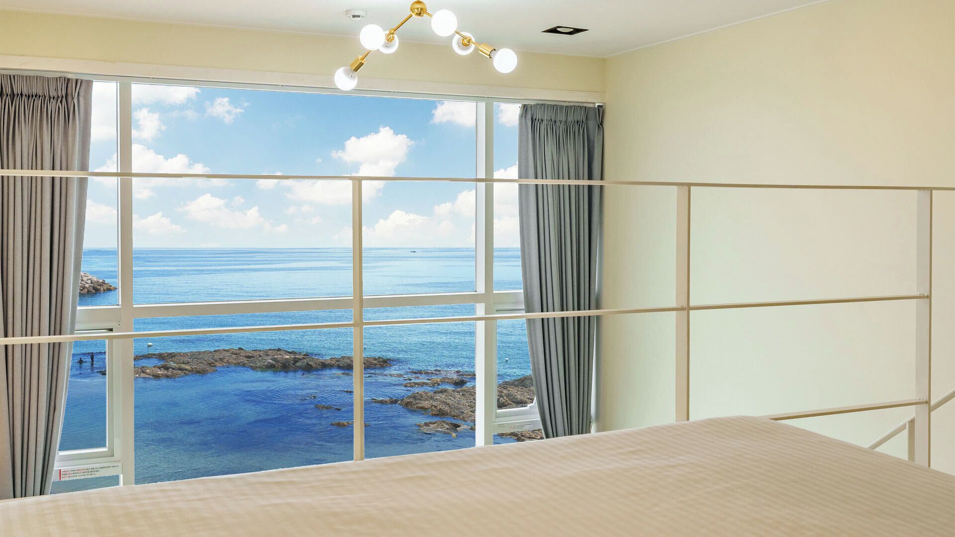 Habitación con un amplio ventanal que ofrece vistas al mar y a la costa rocosa.