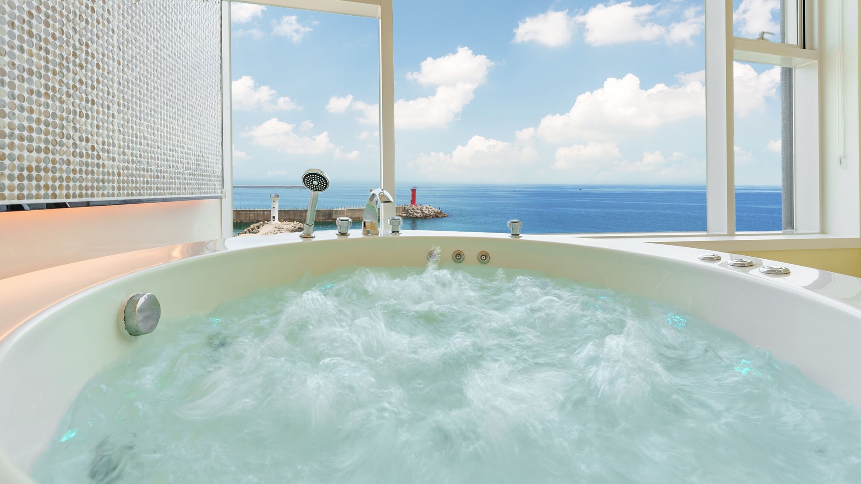 A large bathtub with a view of the sea and a lighthouse.