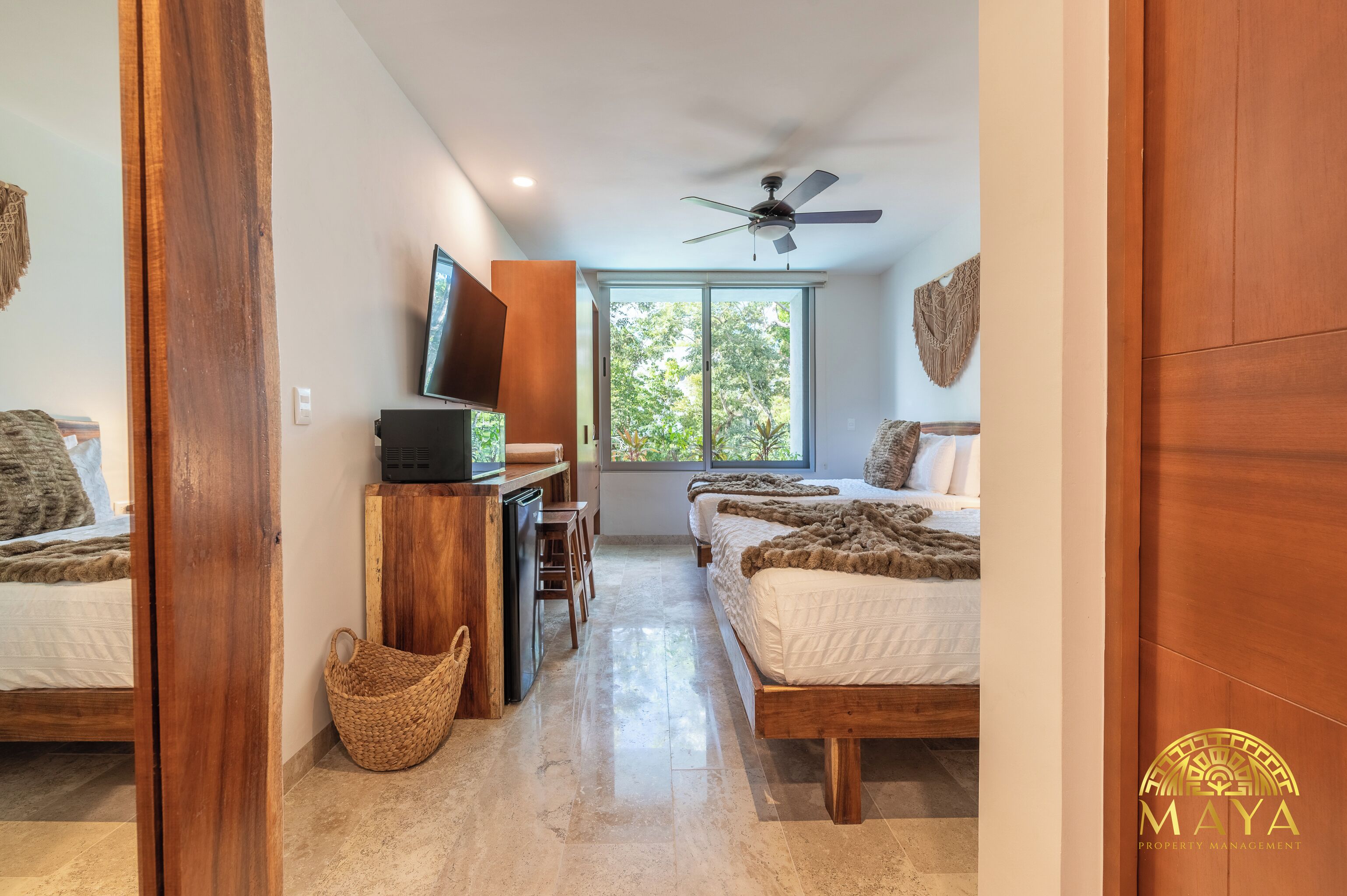 Quarto com cama, escrivaninha, televisão e janela com vista para árvores.