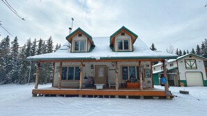 Eine zweistöckige Holzhütte mit Veranda, umgeben von schneebedeckten Bäumen.