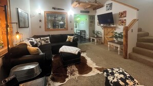 Ein Wohnzimmer mit einer schwarzen Couch, einem Kuhfellteppich und einem aufgehängten Hirschschädel.