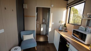 A compact kitchenette with a microwave, sink, and a small dining area with a blue chair.