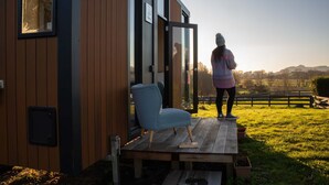A modern house with a wooden exterior, a glass door, and a small porch with a chair and a table.