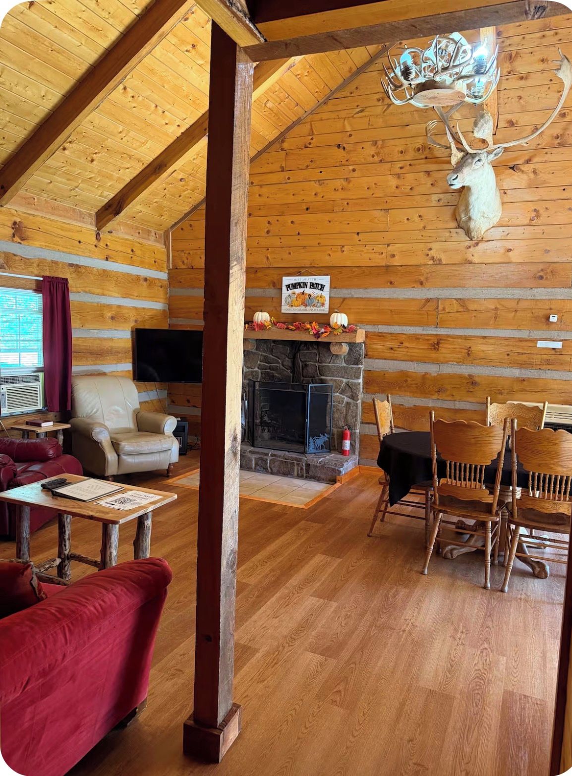 A rustic cabin interior with a stone fireplace, wooden walls, a mounted deer head, and a sign reading 'Pumpkin Patch.'