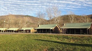 A row of rustic cabins with green roofs, set against a backdrop of hills and a partly cloudy sky. - Charming 3-bedroom 5 bed hottub cabin WiFi in scenic Seneca Rocks West Virginia (Seneca Rocks)