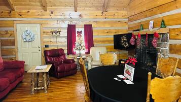 A cozy log cabin interior with a wooden ceiling, a fireplace, a dining table, and a red leather armchair.
