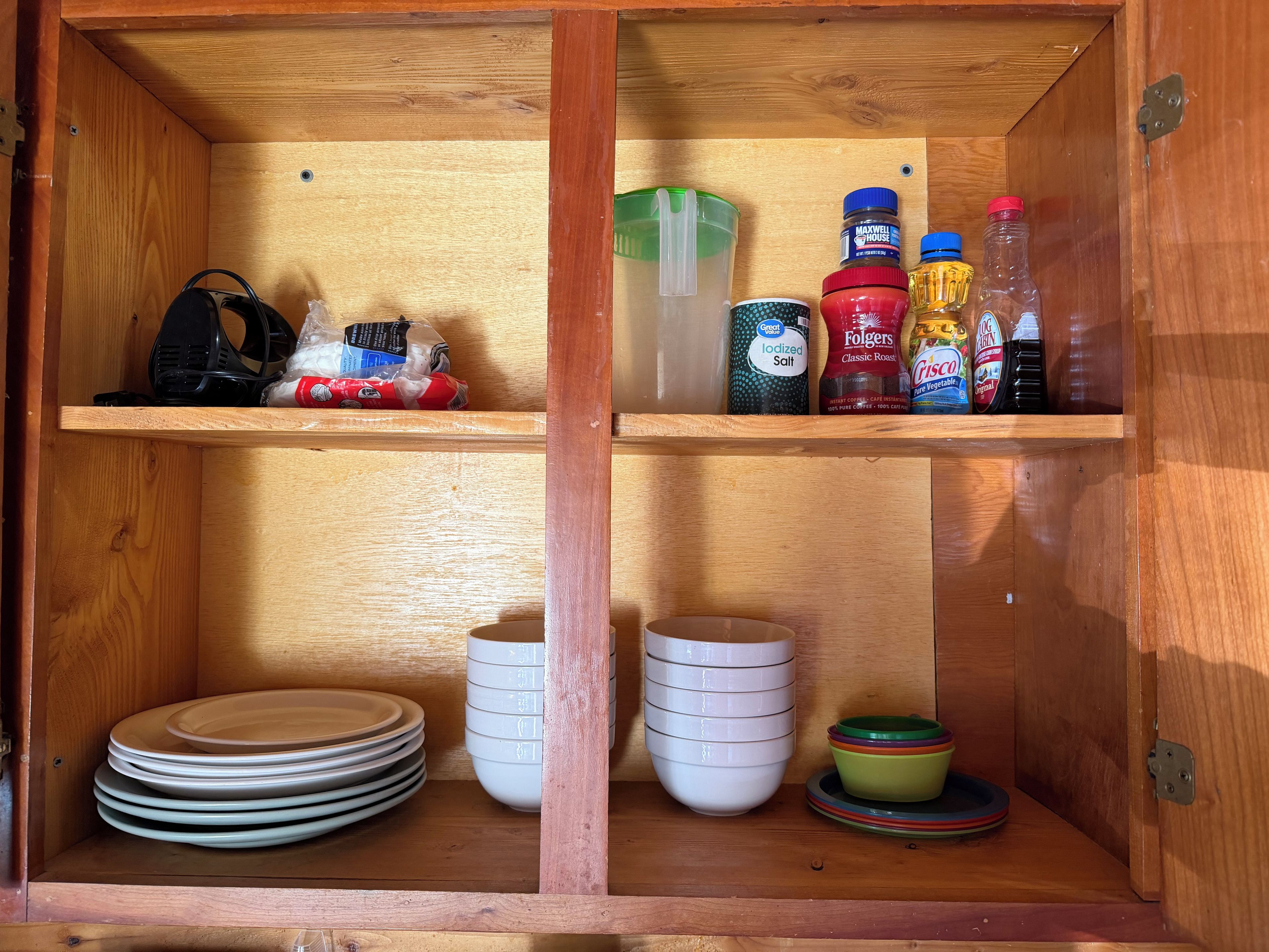 A wooden cabinet with shelves containing kitchenware, a bag of chips, and various condiment bottles.