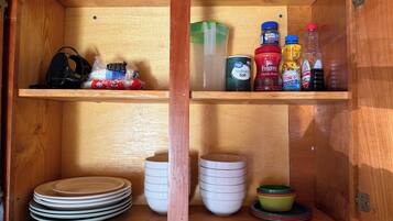 A wooden cabinet with shelves containing kitchenware, a bag of chips, and various condiment bottles.