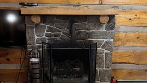 A stone fireplace with a TV above it, a fire extinguisher to the right, and a tiled floor in front. - Charming 3-bedroom 5 bed hottub cabin WiFi in scenic Seneca Rocks West Virginia (Seneca Rocks)
