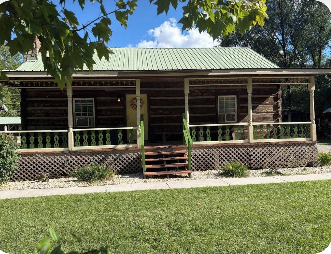 Une cabane en rondins avec une véranda, une porte et une fenêtre.