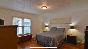 A bedroom with a bed, two bedside tables with lamps, a window with blinds, and a wooden bench. - Charming 3-bedroom house with WiFi, AC in lovely Wichita Falls (Wichita Falls)