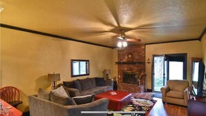 A cozy living room with a fireplace, a ceiling fan, and a large window. - Charming 3-bedroom house with WiFi, AC in lovely Wichita Falls (Wichita Falls)