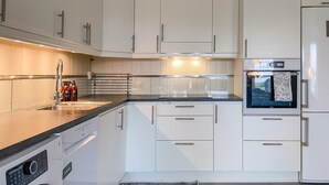 Une cuisine moderne avec des meubles blancs, un four encastré et un lave-linge.