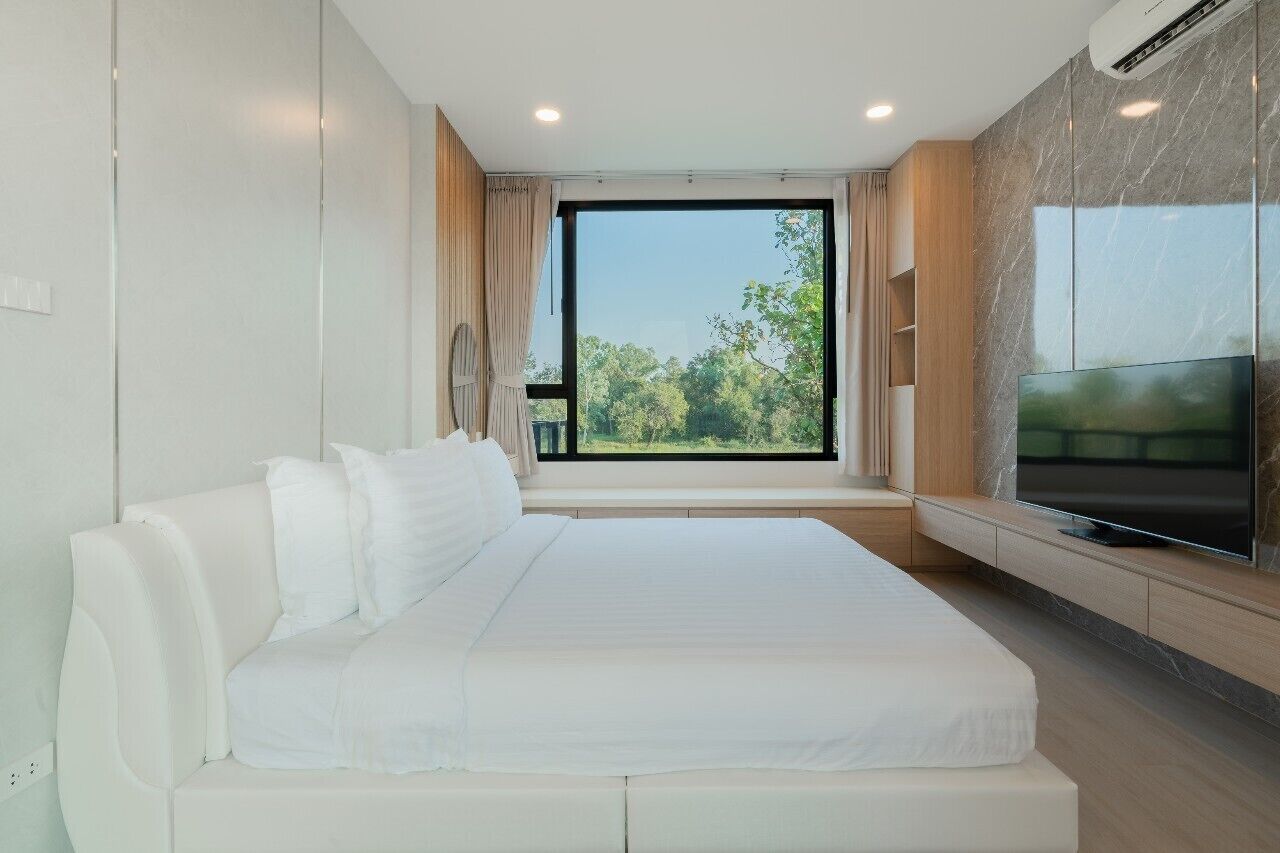 A modern bedroom with a large bed, a TV, and a view of greenery outside.
