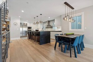 Una cucina moderna con isola centrale, sgabelli da bar, illuminazione a sospensione e un'area pranzo con sedie blu.