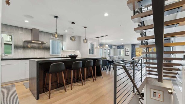 Une cuisine moderne dotée d’un îlot central, de tabourets de bar, de luminaires suspendus et d’un escalier avec une rampe.