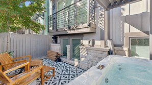 Un jardin avec un jacuzzi, des chaises en bois, une terrasse carrelée et un mur en pierre.