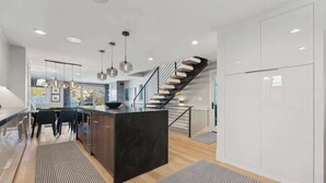 Une cuisine moderne dotée d’un îlot central, d’un escalier et de luminaires suspendus.