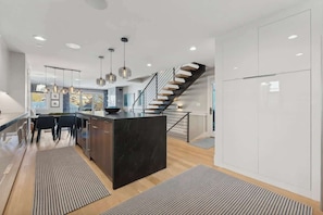 Une cuisine moderne dotée d’un îlot central, d’un escalier et de luminaires suspendus.