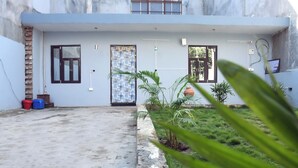 Ein modernes Haus mit flachem Dach, einer Beton-Terrasse und einem kleinen Gartenbereich mit Blumentöpfen.