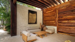 Un espacio de estar al aire libre cubierto, con un sofá, dos sillones y una mesita de centro.